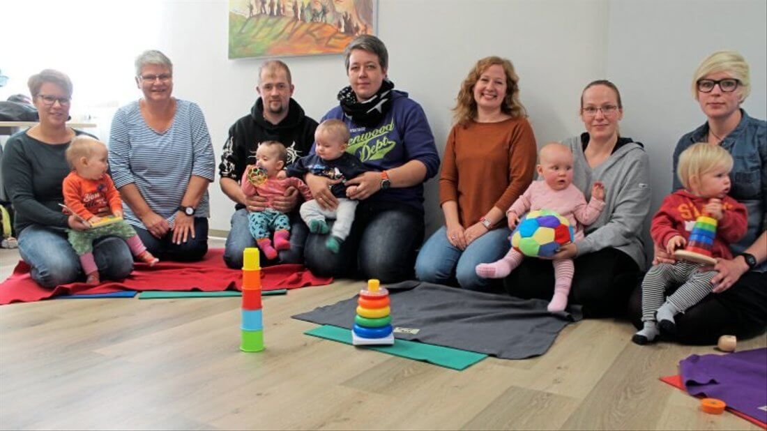 Zwei Betreuerinnen und fünf Eltern mit ihren Kindern sitzen im Halbkreis zusammen für ein Gruppenfoto