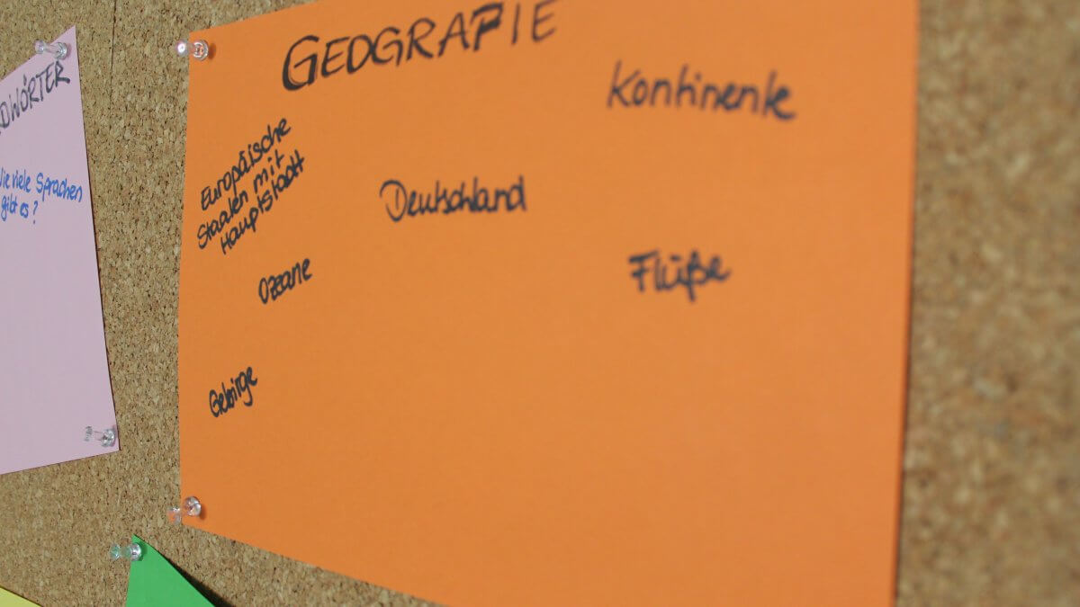 Orangenes Plakat mit Thema Geografie auf Korkwand